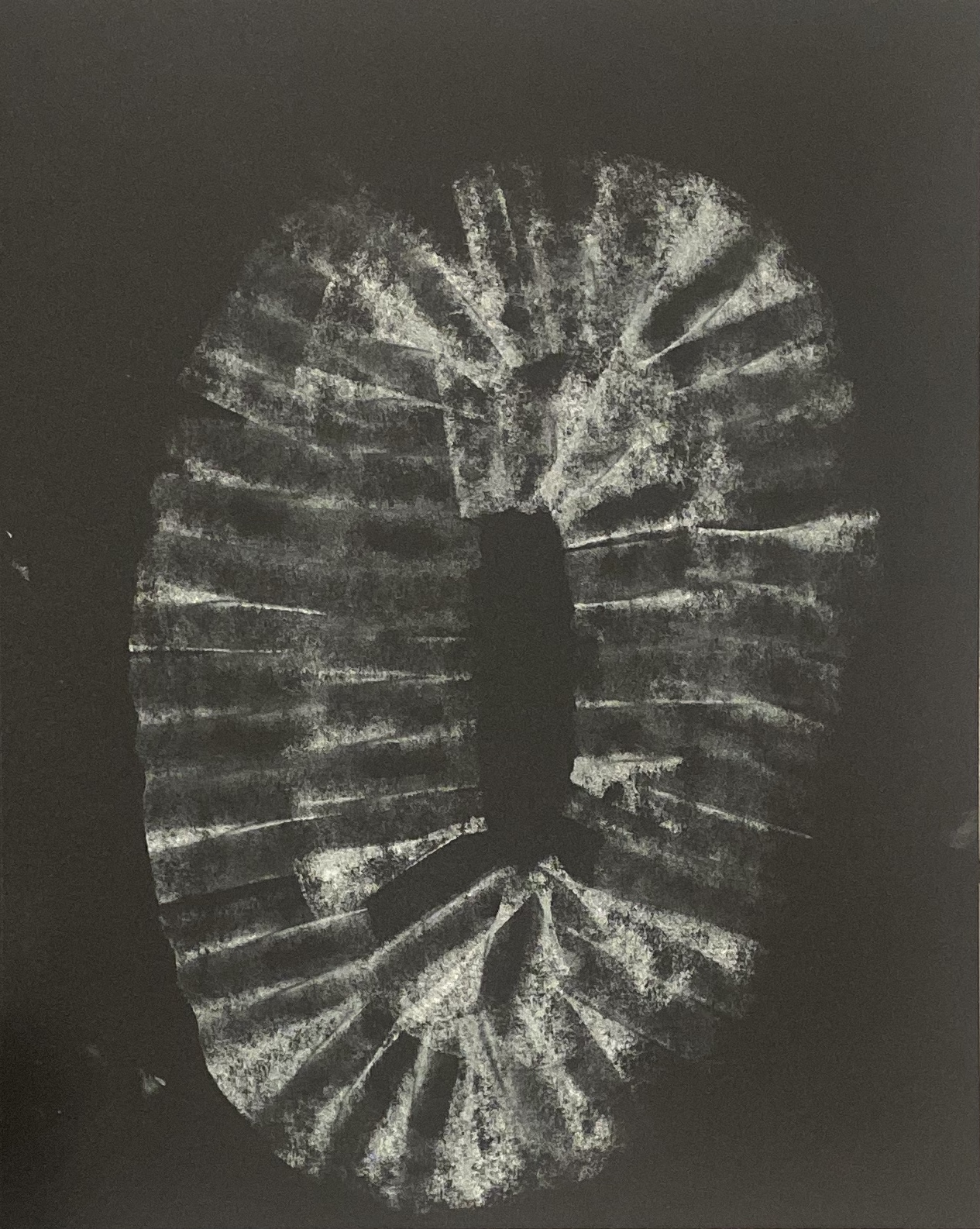 Silver charcoal impression curving around a dark center on black paper