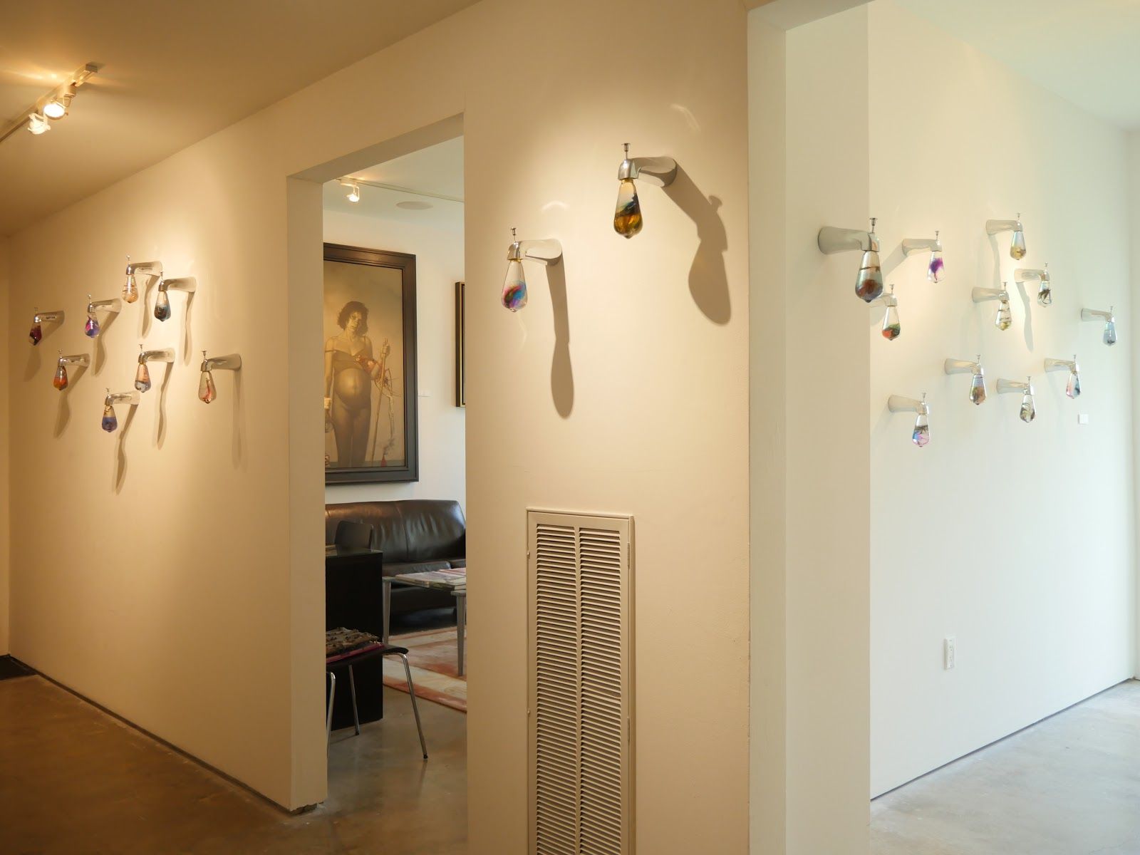 Gallery installation view with clusters of faucet sculptures on white walls on either side of a doorway