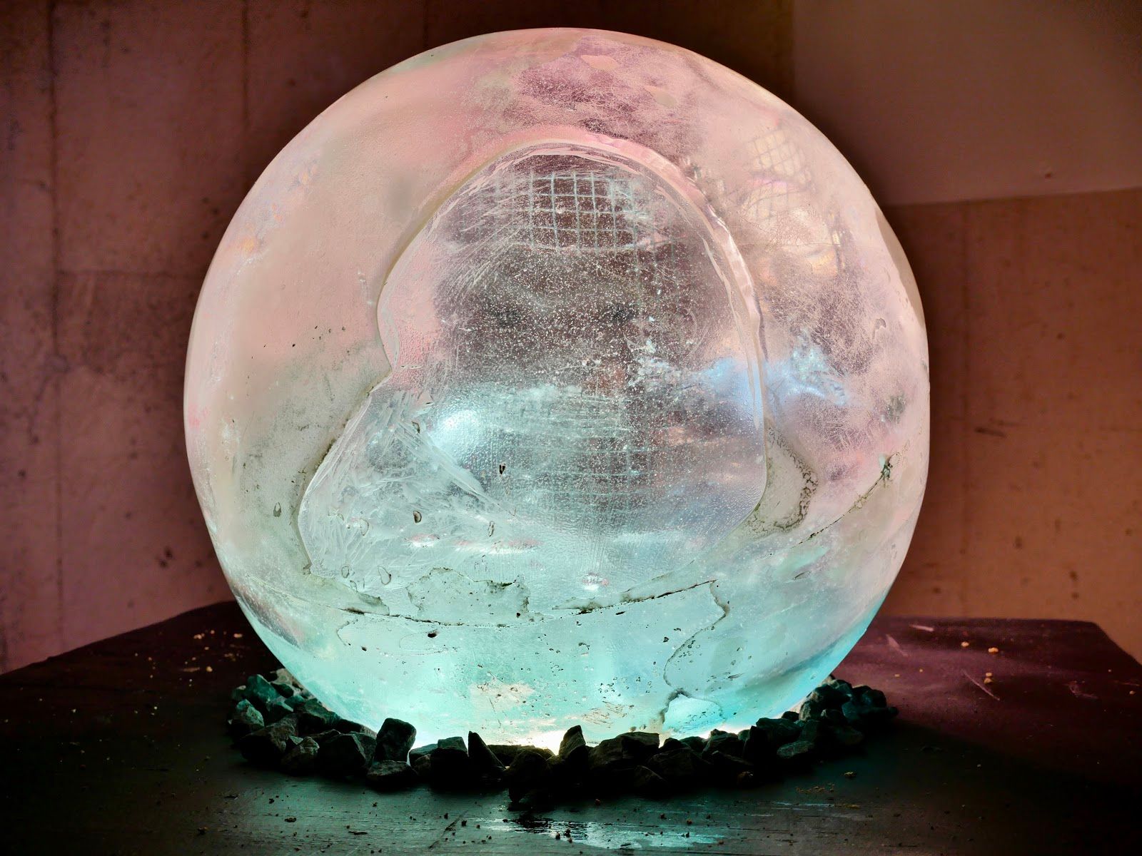 Front view of the giant bulb as a glowing sphere, pale pink and aqua, with wire mesh visible inside