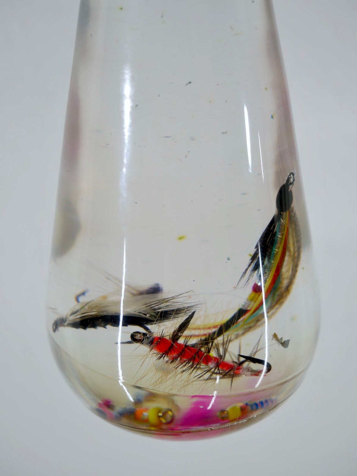Macro detail of a clear resin bulb with a red-bodied fishing fly, black hackle and colored beads