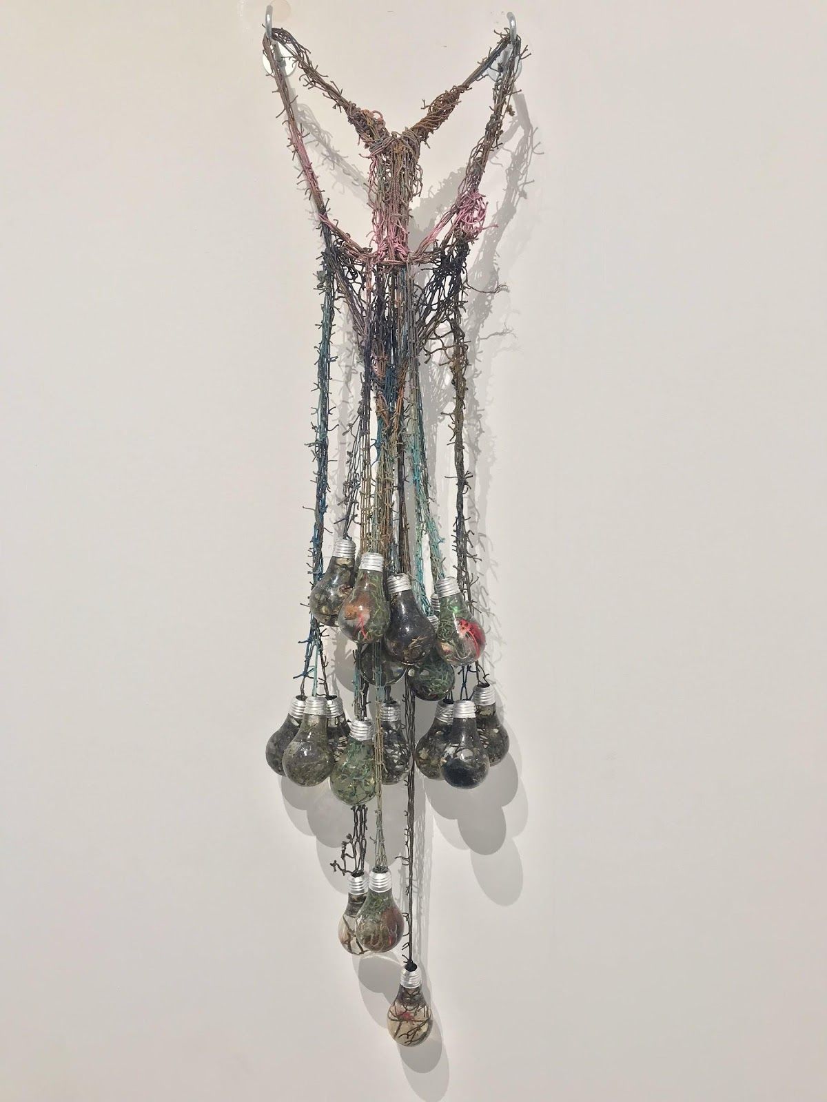 V-shaped wall sculpture of pink, teal and brown painted fishnet gathering into a dense cluster of resin light bulbs